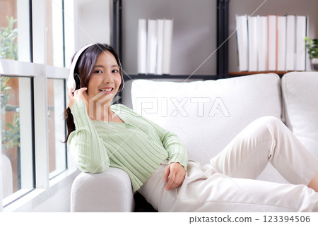 Happy young asian woman wearing headphones listening music while sitting on sofa with fun. Happy young asian woman wearing headphones listening music while sitting on sofa with fun. 123394506
