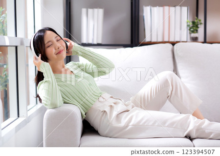 Happy young asian woman wearing headphones listening music while sitting on sofa with fun. Happy young asian woman wearing headphones listening music while sitting on sofa with fun. 123394507