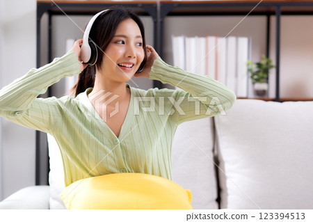 Happy young asian woman wearing headphones listening music while sitting on sofa with fun. 123394513