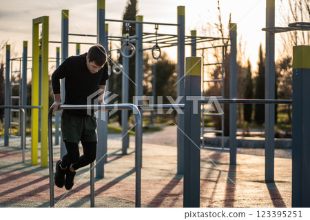 young athletic man exercising fitness calisthenics workout and making dips at street gym during sunset for body improvement and strength training young athletic man exercising fitness calisthenics workout and making dips at street gym during sunset for body improvement and strength training 123395251