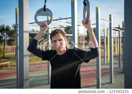 young athletic man resting after fitness calisthenics workout at street gym during sunset, taking a break during body improvement and strength training young athletic man resting after fitness calisthenics workout at street gym during sunset, taking a break during body improvement and strength training 123395255