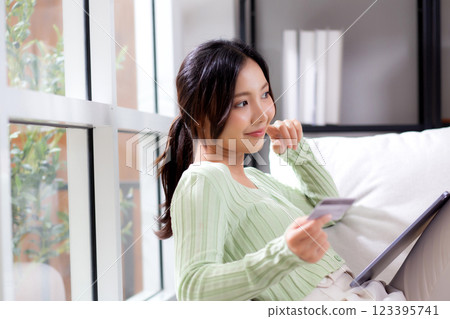 Young asian woman sitting on sofa using tablet computer shopping online with credit card. 123395741