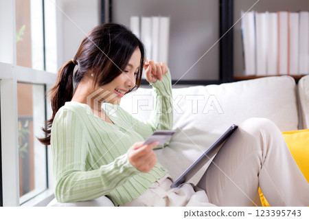 Young asian woman sitting on sofa using tablet computer shopping online with credit card. 123395743