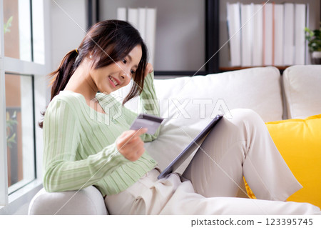 Young asian woman sitting on sofa using tablet computer shopping online with credit card. 123395745