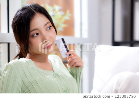 Young asian woman sitting on sofa holding credit card or debit card buying to internet. Young asian woman sitting on sofa holding credit card or debit card buying to internet. 123395750