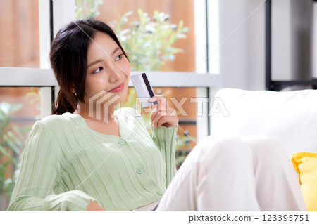 Young asian woman sitting on sofa holding credit card or debit card buying to internet. 123395751