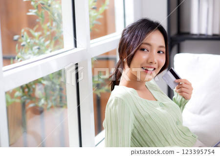Young asian woman sitting on sofa holding credit card or debit card buying to internet. 123395754