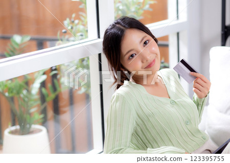 Young asian woman sitting on sofa holding credit card or debit card buying to internet. 123395755