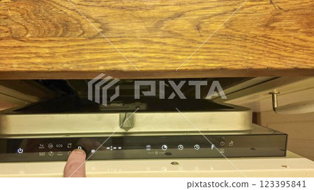 A male finger on the control panel of the dishwasher. Changing cycles on the dishwasher. Illuminated buttons on the dishwasher's digital display. Closing the door of the built-in dishwasher 123395841