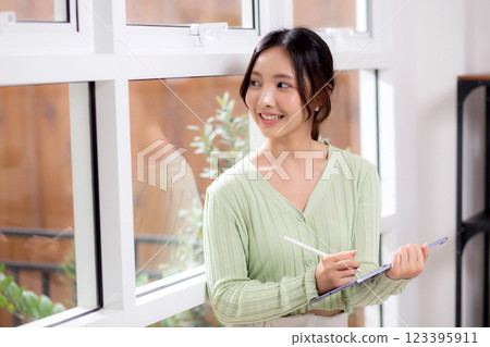 Young asian woman using tablet writing with inspiration and comfortable by window. Young asian woman using tablet writing with inspiration and comfortable by window. 123395911