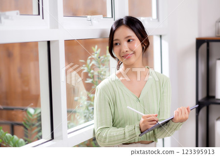 Young asian woman using tablet writing with inspiration and comfortable by window. 123395913