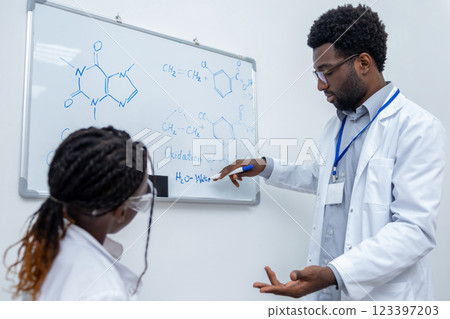 African american man in lab coat standing at the blackboard in a school lab African american man in lab coat standing at the blackboard in a school lab 123397203
