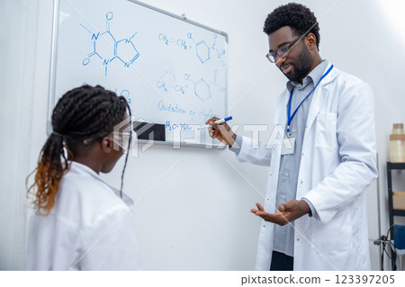 African american man in lab coat standing at the blackboard in a school lab African american man in lab coat standing at the blackboard in a school lab 123397205