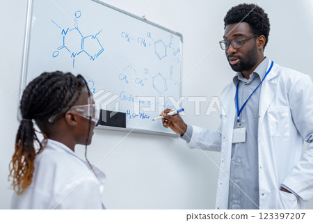 African american school girl standing at the blackboard and listening to the teachers explanations African american school girl standing at the blackboard and listening to the teachers explanations 123397207