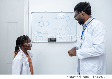 African american school girl standing at the blackboard and listening to the teachers explanations 123397209