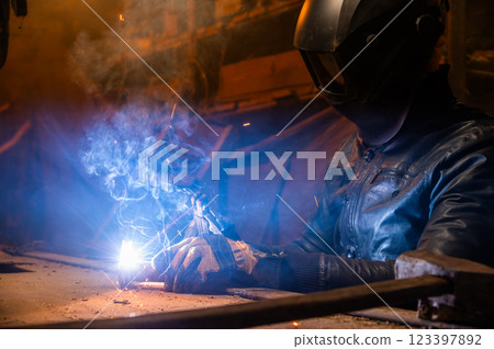 Sculptor uses arc welding to assemble a metal sculpture with proper protection, gloves on and a hard hat. Sparks fly everywhere, hobby 123397892