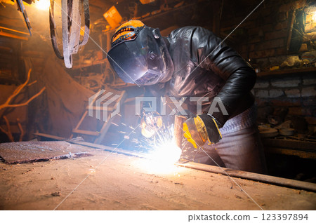 Sculptor uses arc welding to assemble a metal sculpture with proper protection, gloves on and a hard hat. Sparks fly everywhere, hobby 123397894
