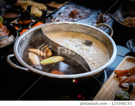 Close-up photo of a stainless steel hot pot divided into two parts, with two different types of soup: a dark, rich soup on one side and a light, clear soup on the other. 123398133