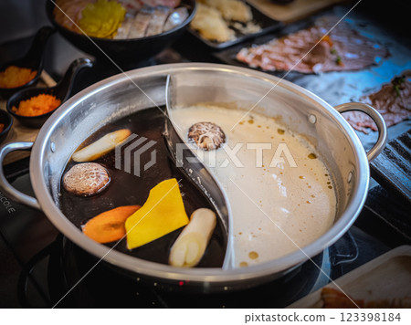 Close-up photo of a stainless steel hot pot divided into two parts, with two different types of soup: a dark, rich soup on one side and a light, clear soup on the other. 123398184