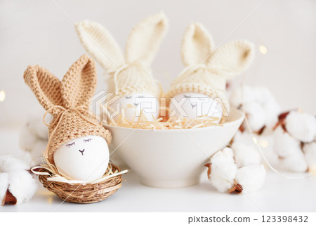 Easter eggs in crochet knitted hats with rabbit ears in nest. Easter celebration concept 123398432