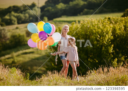 Happy middle-aged woman and young girl with colorful balloons enjoying a sunny day in a green field. Happy middle-aged woman and young girl with colorful balloons enjoying a sunny day in a green field. 123398595