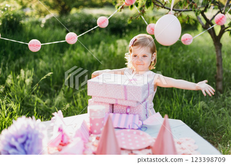 Happy birthday little girl with gift box in beautiful garden. child eat happy birthday rose cupcake. colorful pastel decoration outdoor. 4 years old kid celebrating enjoying party on summer day. 123398709