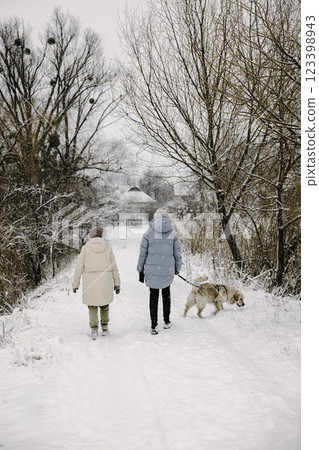 Two women walking a Golden Retriever in a snowy park, enjoying a peaceful winter stroll. 123398943