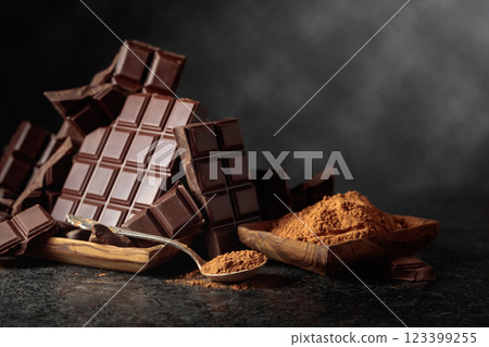Broken dark chocolate bar and cocoa powder on a black background. 123399255