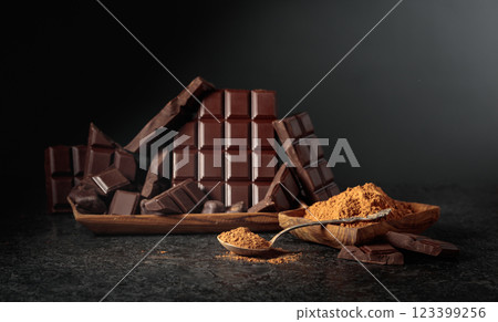 Broken dark chocolate bar and cocoa powder on a black background. Broken dark chocolate bar and cocoa powder on a black background. 123399256