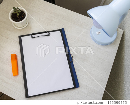 Shot of the plastic folder on the office desk with paper clip holder on the top and other office items. A4 size paper mock up. Shot of the plastic folder on the office desk with paper clip holder on the top and other office items. A4 size paper mock up. 123399553