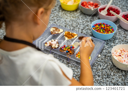 Little girl learning how to cook in a cooking class. Handmade dessert. Making chocolate candy, Child filling heart shaped mold with chocolate Little girl learning how to cook in a cooking class. Handmade dessert. Making chocolate candy, Child filling heart shaped mold with chocolate 123401721