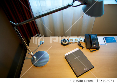Mainz, Germany, July 8, 2017: Hotel Room Desk with Guest Directory, Lamp, and Telephone by Window Mainz, Germany, July 8, 2017: Hotel Room Desk with Guest Directory, Lamp, and Telephone by Window 123402074