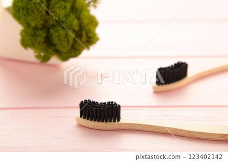 Bamboo wood toothbrush with black brush bristles on pink background 123402142