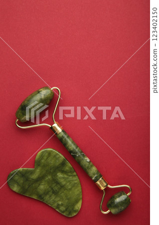 Green jade roller and gua sha stone for facial massage and on pink background. Home beauty and selfcare accessories. Face roller for anti age wrinkle treatment. Top view, flat lay. Green jade roller and gua sha stone for facial massage and on pink background. Home beauty and selfcare accessories. Face roller for anti age wrinkle treatment. Top view, flat lay. 123402150