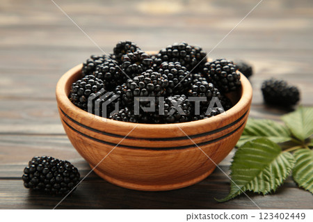 Ripe blackberries with leaves in a wooden bowl on brown wooden background. Ripe blackberries with leaves in a wooden bowl on brown wooden background. 123402449