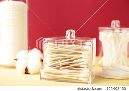 Cotton pads and cotton sticks in containers with cotton flower on red background. Cotton pads and cotton sticks in containers with cotton flower on red background. 123402460