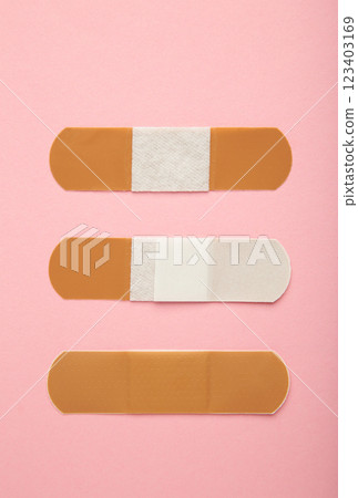 Beige adhesive bandages on pink background. Medical plasters. Vertical photo 123403169
