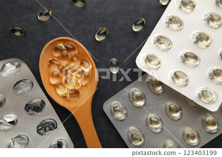Vitamin D yellow pills on wood spoon on dark background. Medicine tablets of vitamin d on table. Vitamin D yellow pills on wood spoon on dark background. Medicine tablets of vitamin d on table. 123403199