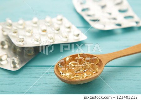 Vitamin D yellow pills on wood spoon on blue background. Medicine tablets of vitamin d on table. 123403212