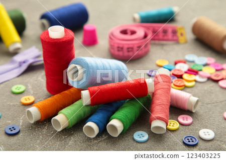 Sewing supplies on grey background: sewing thread, scissors, a large spool of thread, pieces of cloth, needles,centimeter, buttons. 123403225