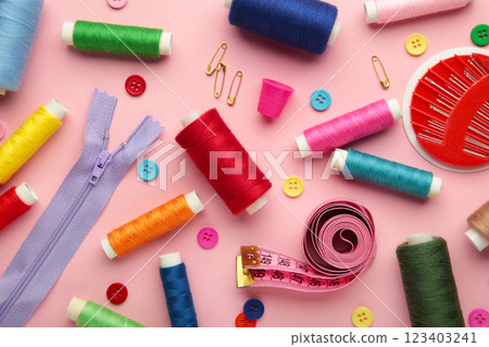 Sewing supplies on pink background: sewing thread, scissors, a large spool of thread, pieces of cloth, needles,centimeter, buttons Sewing supplies on pink background: sewing thread, scissors, a large spool of thread, pieces of cloth, needles,centimeter, buttons 123403241