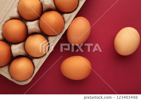 Chicken eggs in an open egg carton on red background. Top view with copy space. Natural healthy food and organic farming concept. Chicken eggs in an open egg carton on red background. Top view with copy space. Natural healthy food and organic farming concept. 123403498