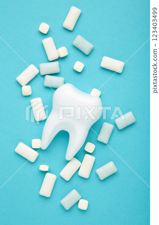 White healthy tooth model and heap of chewing gums on blue background. Concept of oral dental hygiene Vertical photo White healthy tooth model and heap of chewing gums on blue background. Concept of oral dental hygiene Vertical photo 123403499