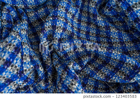 A close-up of folded boucle blue and black checkered fabric with detailed texture and soft folds 123403583