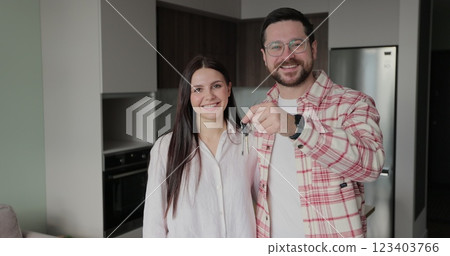 Happy couple owners of a new apartment show the key looking at the camera. Buying first family real estate, move in new home. Home buying concept. 123403766