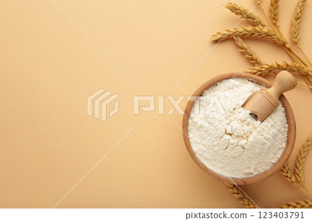 Wooden bowl with flour and spikelets of wheat. Wheat flour on beige background. Top view. 123403791