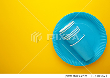 Eco-friendly disposable utensils made of craft paper on yellow background. Blue plates and paper cups Eco-friendly disposable utensils made of craft paper on yellow background. Blue plates and paper cups 123403871