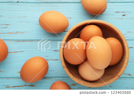 Top view of raw brown eggs on wooden bawl on blue wooden background. Eggs are a common ingredient in cooking. Top view of raw brown eggs on wooden bawl on blue wooden background. Eggs are a common ingredient in cooking. 123403880