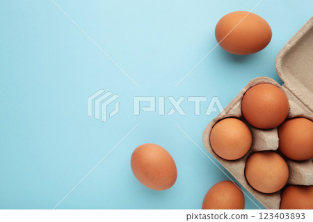 Chicken eggs in an open egg carton on blue. Top view with copy space. Natural healthy food and organic farming concept. Chicken eggs in an open egg carton on blue. Top view with copy space. Natural healthy food and organic farming concept. 123403893