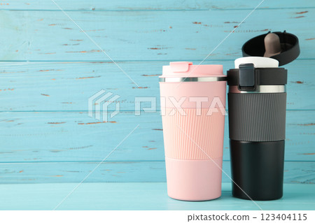 Two thermo cups or thermos mugs for tea or coffee on blue background. Black and pink for him and her. Hot beverage for couples 123404115
